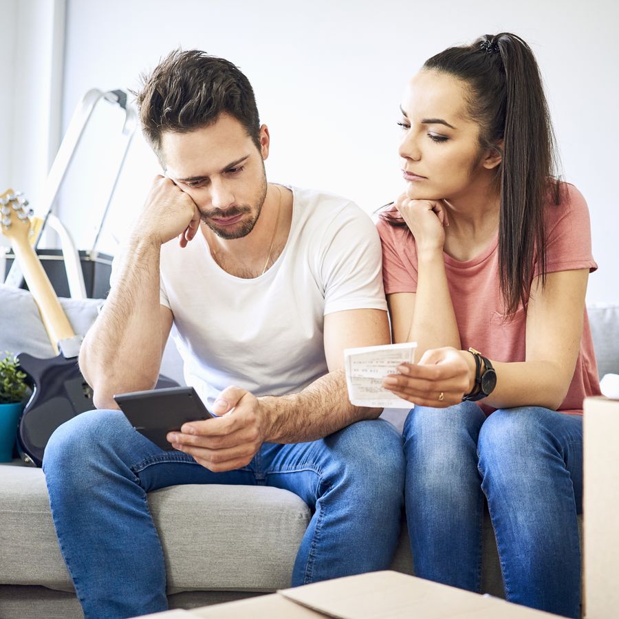Man looking at a phone and woman holding a piece of paper while they sit on the couch